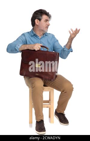 Smart casual man explaining and gesturing, holding his briefcase while sitting on a chair on white studio background Stock Photo