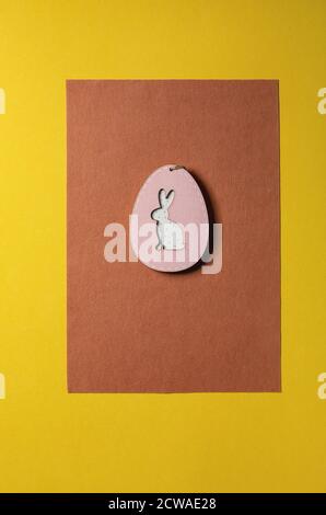 Minimal Easter greeting card with wooden decoration egg with rabbit inside on bright felt orange yellow background. Flat lay, copy space. Stock Photo