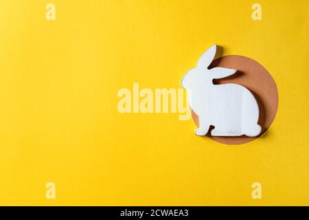 Easter minimal greeting card with white wooden rabbit decoration on bright paper yellow background. Flat lay, copy space. Stock Photo