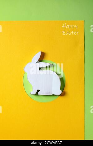 Easter minimal greeting card with white wooden rabbit decoration on bright paper yellow green background. Happy Easter inscription. Flat lay, copy spa Stock Photo