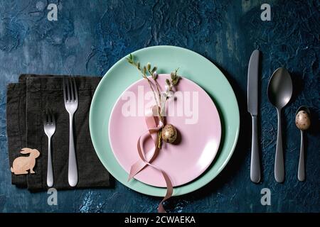 Easter table setting with cutlery and empty plates with blossom willow branches and golden quail egg. Classic blue texture background. Flat lay, space Stock Photo