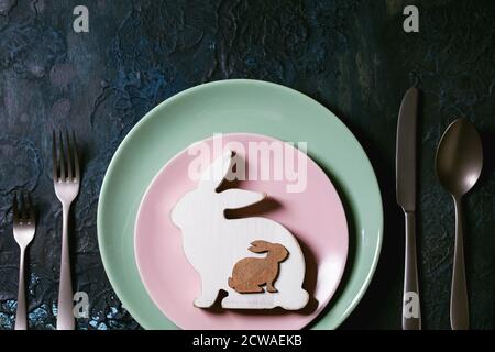 Easter table setting with cutlery and empty plates with wooden Easter decoration white bunny rabbit and golden quail eggs. Classic blue texture backgr Stock Photo