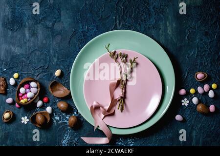 Easter table setting with chocolate eggs, candies and empty plates with blossom willow branches. Classic blue texture background. Flat lay, space Stock Photo