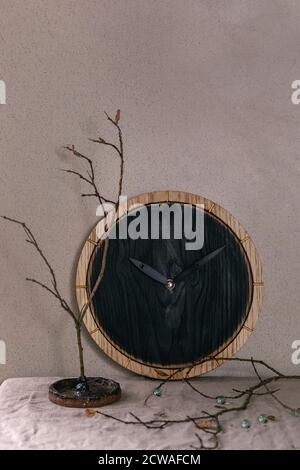 Wall black burned round wooden clocks on table with grey linen tablecloth and dry branches. Interior design Stock Photo