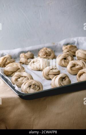 Ready to bake traditional Swedish cardamom sweet buns Kanelbulle on oven tray cover by baking paper on grey linen table cloth. Stock Photo
