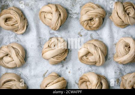 Ready to bake traditional Swedish cardamom sweet buns Kanelbulle on oven tray cover by baking paper. Flat lay, space Stock Photo