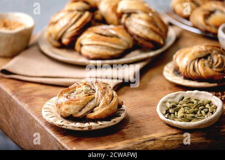 Traditional Swedish cardamom sweet buns Kanelbulle on plate, ingredients in ceramic bowl above on wooden table. Stock Photo