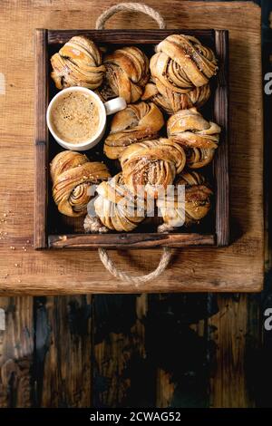 Traditional Swedish cardamom or cinnamon sweet buns Kanelbulle in wooden tray, cup of coffee on wooden table. Flat lay, space Stock Photo