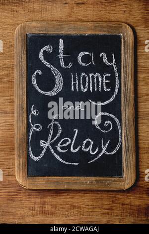 Stay home quarantine isolation period concept. Vintage chalkboard with handwritten chalk lettering Stay home and relax. Wooden background Stock Photo