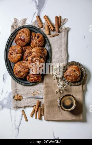 Traditional Swedish cinnamon sweet buns Kanelbulle on vintage tray, cup of coffee, cinnamon sticks, blossom branches on linen cloth over white texture Stock Photo