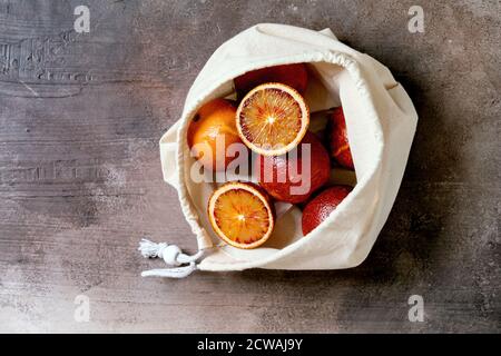 Blood sicilian oranges, ripe and juicy, in cotton eco friendly bag, whole and sliced, over grey concrete background. Flat lay, space Stock Photo