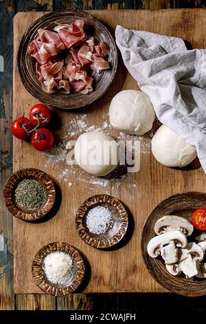 Dough for pizza napolitana cooking. Three balls of fresh homemade wheat dough, prosciutto and ingredients in ceramic plates above on wooden table. Hom Stock Photo