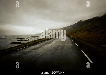 Driving in wet weather an empty Icelandic coastal road in the Westfjord coastline landscape of North West Iceland. Stock Photo