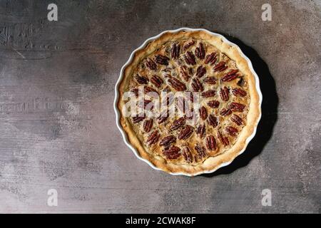Fresh home baking classic american pecan caramel pie in white ceramic baking dish over grey texture background. Flat lay, space Stock Photo