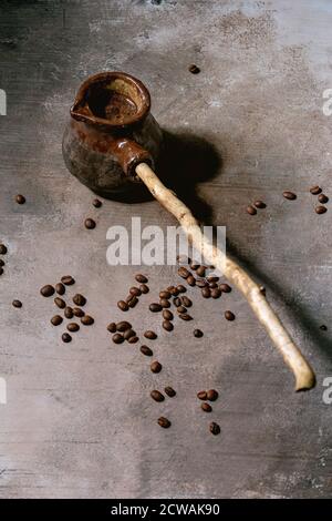 Black turkish coffee in craft handmade ceramic coffee pot cezve with long wooden handle with coffee beans above. Grey texture background. Copy space Stock Photo