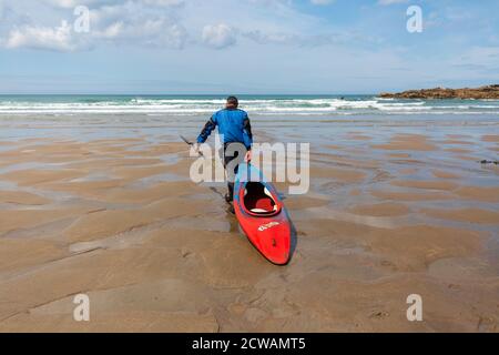 Man pulling his canoe along the beach towards the sea Stock Photo