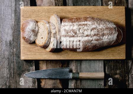 Sliced whole grain artisan rye-wheat organic bread on wood cutting board, big knife over old wooden background. Flat lay, space Stock Photo