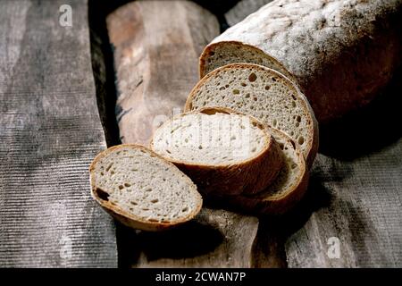 Sliced whole grain artisan rye-wheat organic bread over old wooden background. Stock Photo