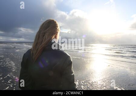 Middle aged white caucasian woman on the beach at Troon, Ayrshire with approaching storm looking out toward the weather front,walking on the beach feeling melancholic & thoughful. A concept image designed for a cover or to show melacholy, loneliness. lost love Stock Photo