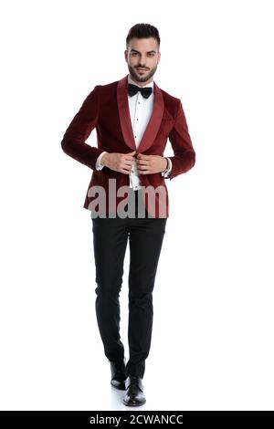 smiling young man in red velvet tuxedo adjusting coat and walking isolated on white background, full body Stock Photo