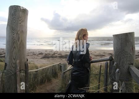 Middle aged white caucasian woman on the beach at Troon, Ayrshire with approaching storm looking out toward the weather front,walking on the beach feeling melancholic & thoughful. A concept image designed for a cover or to show melacholy, loneliness. lost love Stock Photo