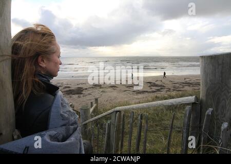 Middle aged white caucasian woman on the beach at Troon, Ayrshire with approaching storm looking out toward the weather front,walking on the beach feeling melancholic & thoughful. A concept image designed for a cover or to show melacholy, loneliness. lost love Stock Photo