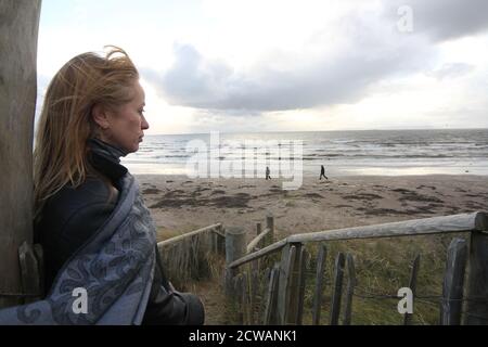 Middle aged white caucasian woman on the beach at Troon, Ayrshire with approaching storm looking out toward the weather front,walking on the beach feeling melancholic & thoughful. A concept image designed for a cover or to show melacholy, loneliness. lost love Stock Photo