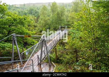 A lone visitor braves the heavy rain on the Suspension bridge over the Corrieshalloch Gorge, Wester Ross, Highland Region, Scotland, UK Stock Photo