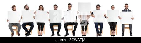 Team of 9 businessmen holding empty billboards while one is hiding her face and other one is yelling, sitting on chairs on white studio background Stock Photo
