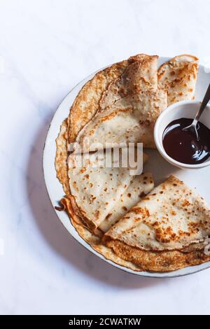 Small stack of crepes folded in triangle on a large plate with a small bowl of dark chocolate sauce. Stock Photo