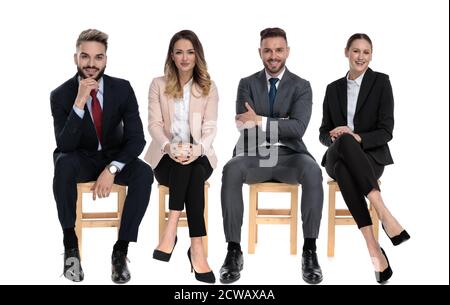 Team of 4 positive businessmen smiling while sitting on chairs on white studio background Stock Photo