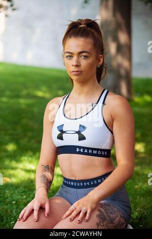 A young woman wearing sportswear sitting down in the shade of a tree outside. Stock Photo