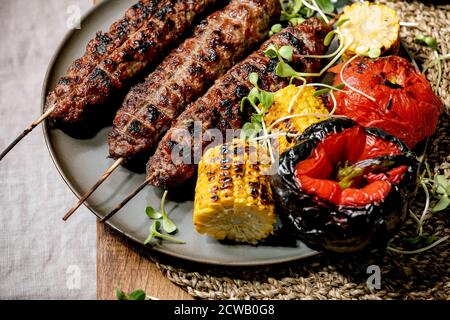 Eastern fast food. Grilled spicy beef lyulya kebab on sticks on flat bread with grilled vegetables sweet corn cob, tomato and paprika, tomato sauce on Stock Photo