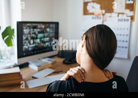 Young Woman with neck pain after long working hours in home office. Release tension in your neck. Stock Photo