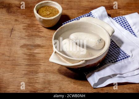 Munich Bavarian traditional white sausages in ceramic pan served with german sweet mustard on white and blue napkin over wooden background. Stock Photo