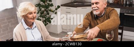 panoramic shot of joyful senior man pouring white wine during thanksgiving dinner with wife Stock Photo