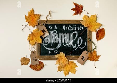 Autumn sale concept. Vintage chalkboard with hand written lettering Sale, labels with percents, yellow autumn leaves over beige background. Flat lay. Stock Photo