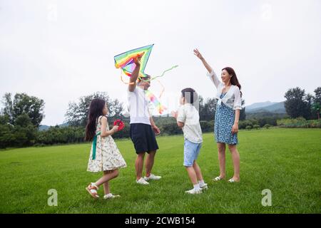 The happy family of four is flying a kite on the grass Stock Photo
