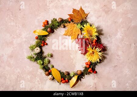 Beautiful Autumn botanical wreath composition creative layout with flowers, moss and yellow autumn leaves over beige concrete background. Flat lay, co Stock Photo