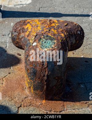 Closeup of an old rusty mooring post on the waterfront in a small marina, element for mooring ships in the harbor, safety Stock Photo