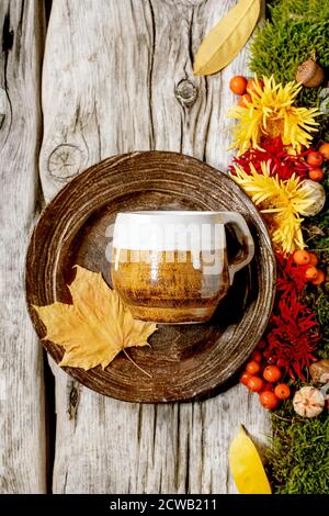 Autumn holidays table setting. Empty craft ceramic plate and mug on old wooden table decorated by fall yellow leaves, autumn berries, moss and flowers Stock Photo