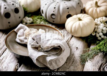 Holiday table setting decoration with white decorative pumpkins, craft clay pumpkins, thuja branches, empty plate with cloth napkin over old wooden ta Stock Photo