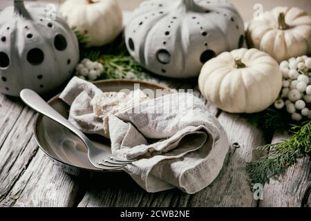 Holiday table setting decoration with white decorative pumpkins, craft clay pumpkins, thuja branches, empty plate with cloth napkin, cutlery over old Stock Photo