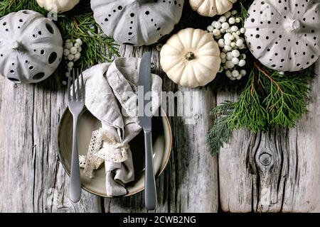 Holiday table setting decoration with white decorative pumpkins, craft clay pumpkins, thuja branches, empty plate with cloth napkin, cutlery over old Stock Photo
