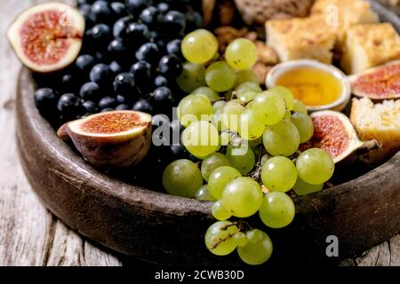 Wine appetizers with different grapes, figs, walnuts, bread, honey and goat cheese on ceramic plate over old wooden background. Close up Stock Photo