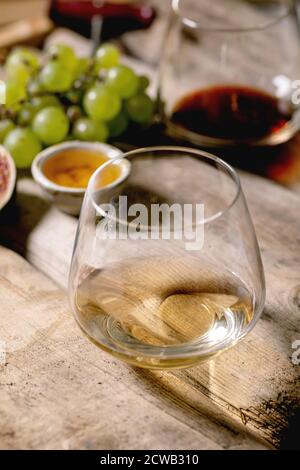 Glasses of red and white wine with grapes, figs, goat cheese and walnuts over old wooden background. Close up Stock Photo