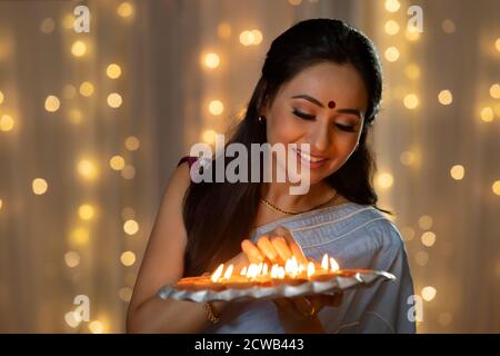 Woman decorating a plate with diyas in her hand Stock Photo
