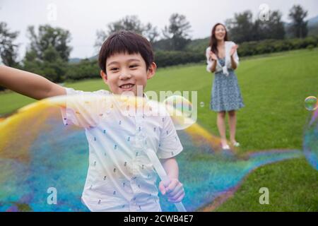 Happy mother and child playing on the grass blowing bubbles Stock Photo