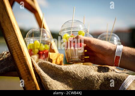 Hand takes fresh fruit pieces salad in plastic glass Stock Photo