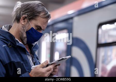 Moscow. Russia. September 28, 2020. A man in a protective medical mask stands on the platform of a subway station and carefully reads a newspaper. The Stock Photo